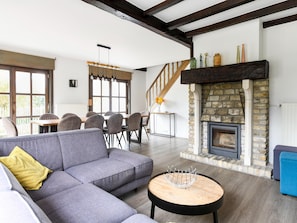 A modern living room with a grey sectional sofa, a round coffee table, a stone fireplace, and a wooden staircase. - Holiday Home Nieuwpoort Near Sandy Beach (Nieuwpoort)