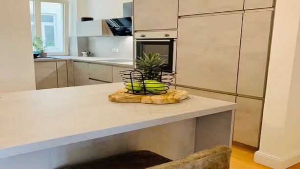 Une cuisine moderne avec un plan de travail blanc, un four encastré et un petit coin repas agrémenté d’une banquette.
