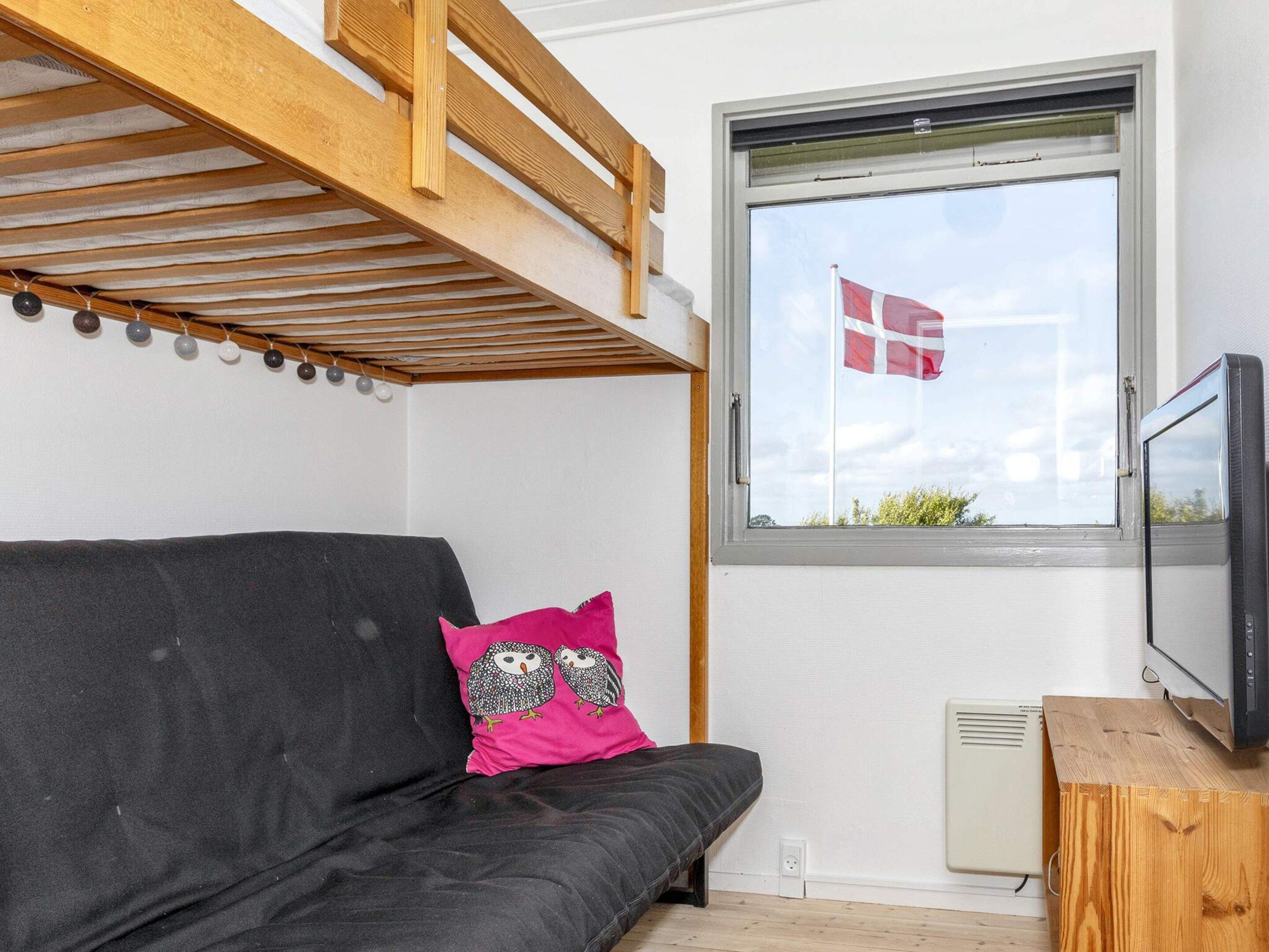 A room with a bunk bed, a window with a flag, a television, and a sofa with decorative pillows.