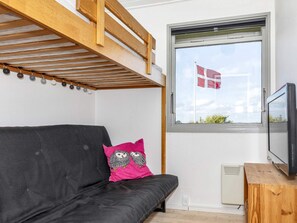 Une chambre avec un lit superposé, une fenêtre ornée d’un drapeau, une télévision et un canapé agrémenté de coussins décoratifs.
