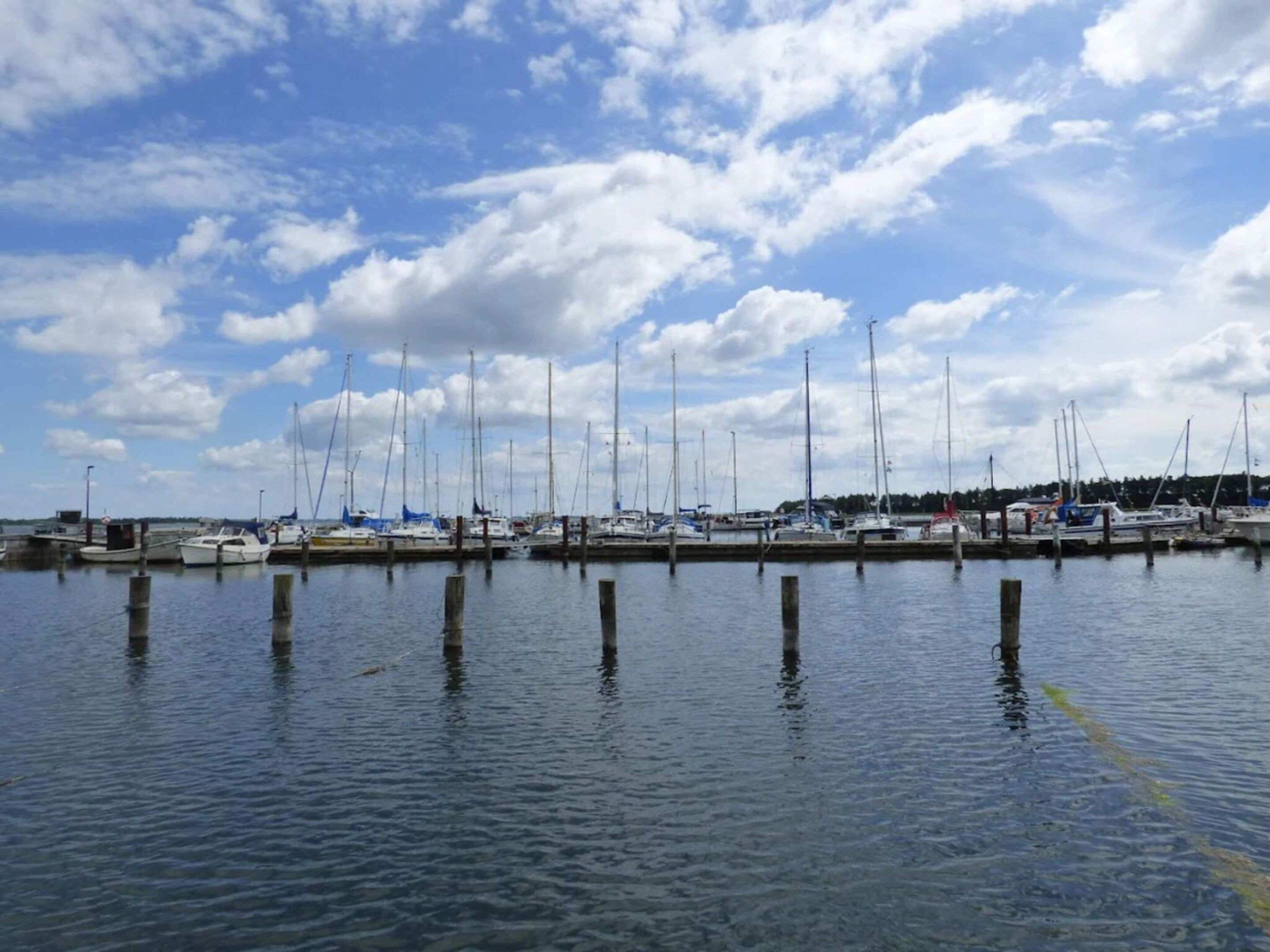 A marina with multiple boats docked, calm water, and a partly cloudy sky.