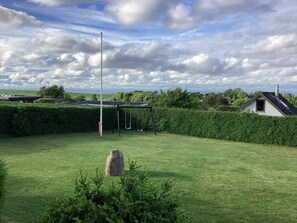 A grassy outdoor area with a swing set, a tall flagpole, and a stone structure. - 5 Person Holiday Home in Roslev (Roslev)