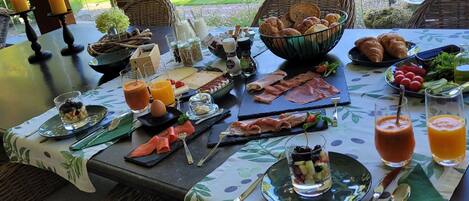 An outdoor dining area with a table set for breakfast, including bread, pastries, meats, and beverages.