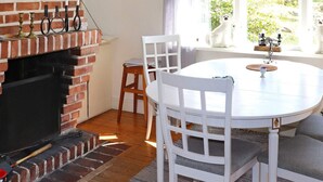 A cozy room with a brick fireplace, white chairs, a round table, and a view of greenery through a window. - 5 Person Holiday Home in Falkenberg (Falkenberg)