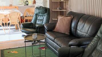 A living room with a leather sofa, a green chair, a small round table, and a bookshelf.