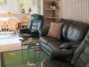 Ein Wohnzimmer mit einer Ledersofa, einem grünen Sessel, einem kleinen runden Tisch und einem Bücherregal.