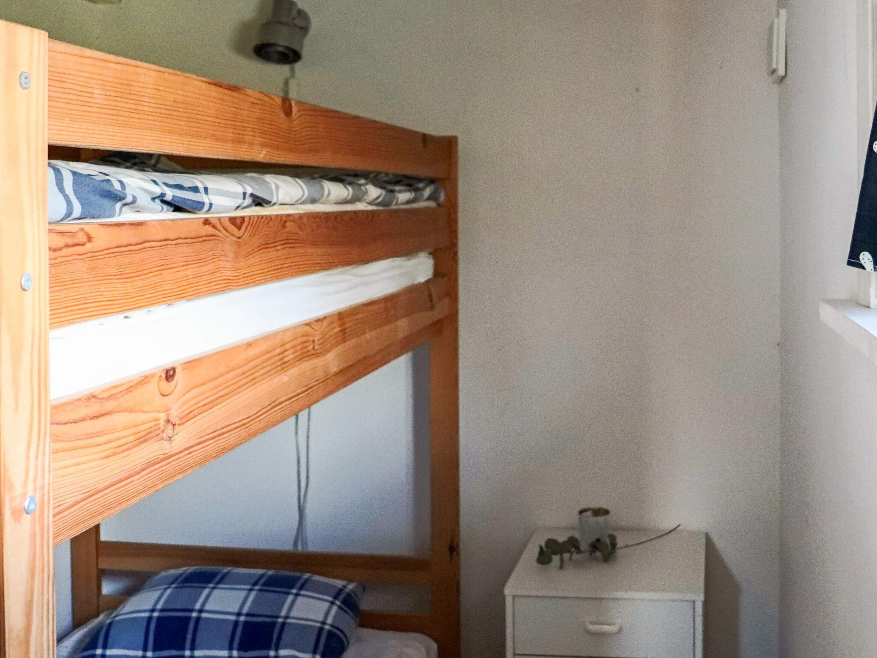 Un lit superposé avec une structure en bois, une table de chevet blanche avec un tiroir et un luminaire fixé au mur.