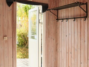 Un intérieur en bois avec une porte donnant sur un espace extérieur, un présentoir en métal noir et un tableau de distribution électrique.