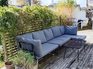 Une terrasse en bois avec un canapé gris et une petite table.