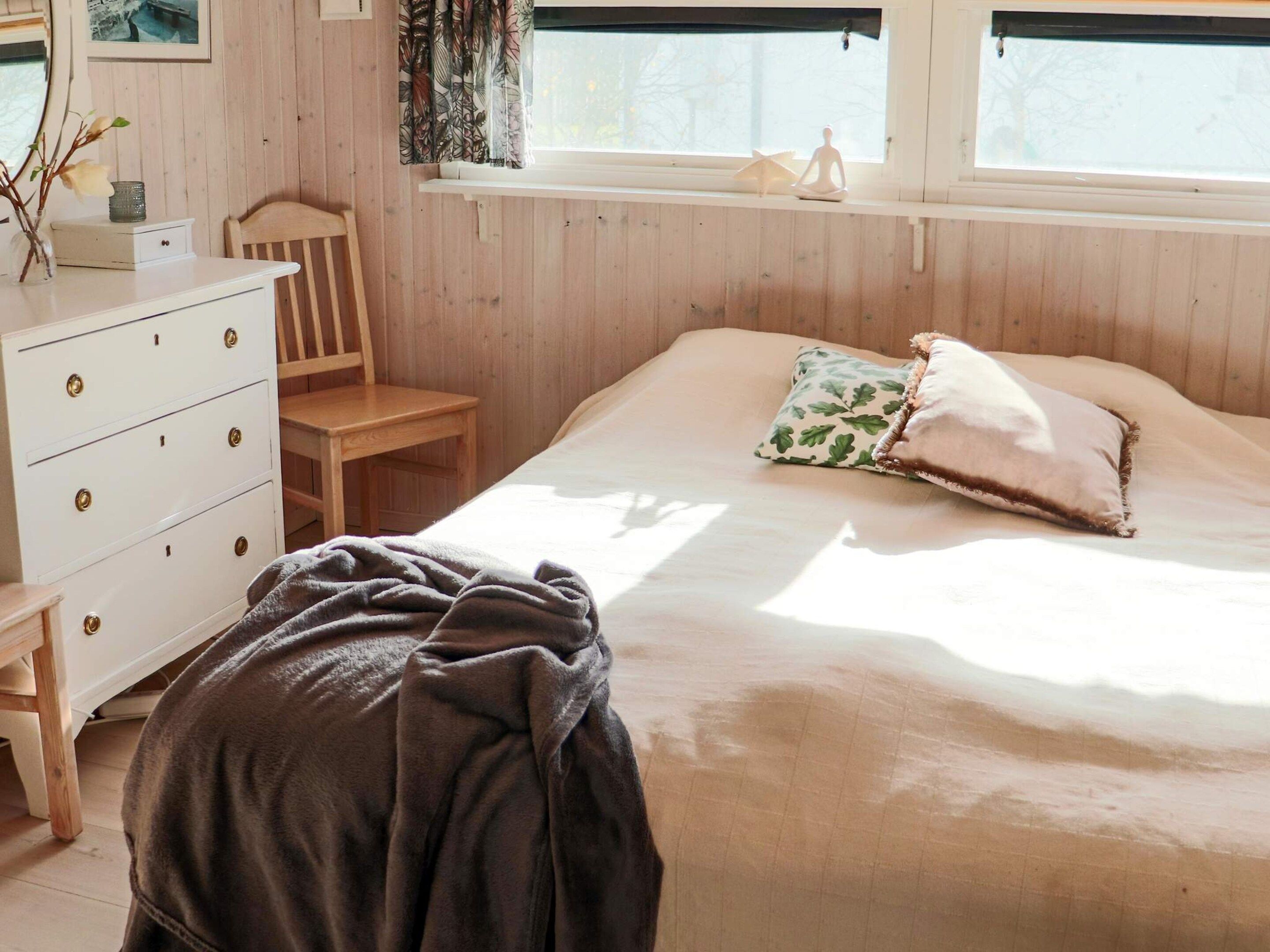 A bedroom with a bed, a wooden dresser, a chair, and a window with curtains.