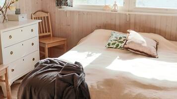 A bedroom with a bed, a wooden dresser, a chair, and a window with curtains.