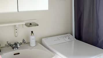 A bathroom with a sink, a bottle of lotion, and a washing machine.