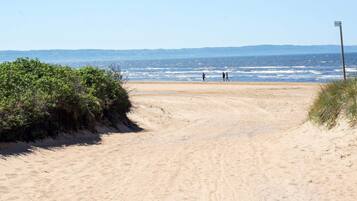 A sandy beach path leading to the sea with a few people walking.