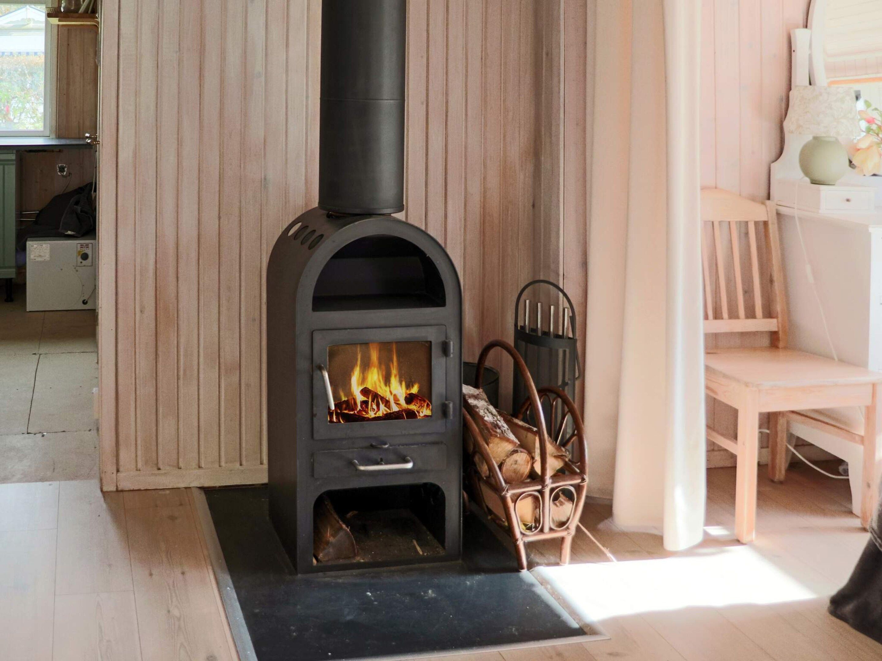 Un poêle à bois avec un feu, une chaise et un banc dans une pièce aux murs et au plancher en bois.