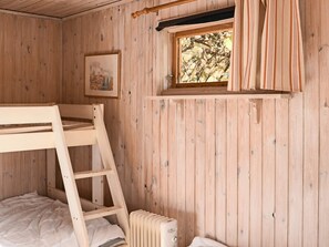 Et værelse med køjeseng i træ, en stige, en radiator, et vindue med gardiner og et billede i ramme på væggen.