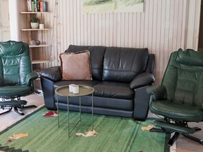 Un salon avec un canapé en cuir noir, deux fauteuils en cuir vert, une petite table ronde et un tapis vert orné d’un motif de cygne.