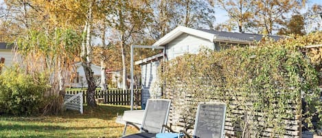 A garden with two lounge chairs, a wooden fence, and a house in the background.