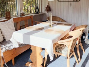 A dining area with a wooden table set for four, surrounded by wicker chairs, a bench, and a window with plants.