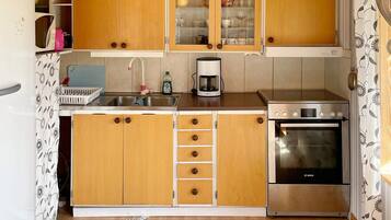 A compact kitchen with wooden cabinets, a stainless steel sink, a Bosch oven, and a coffee maker.