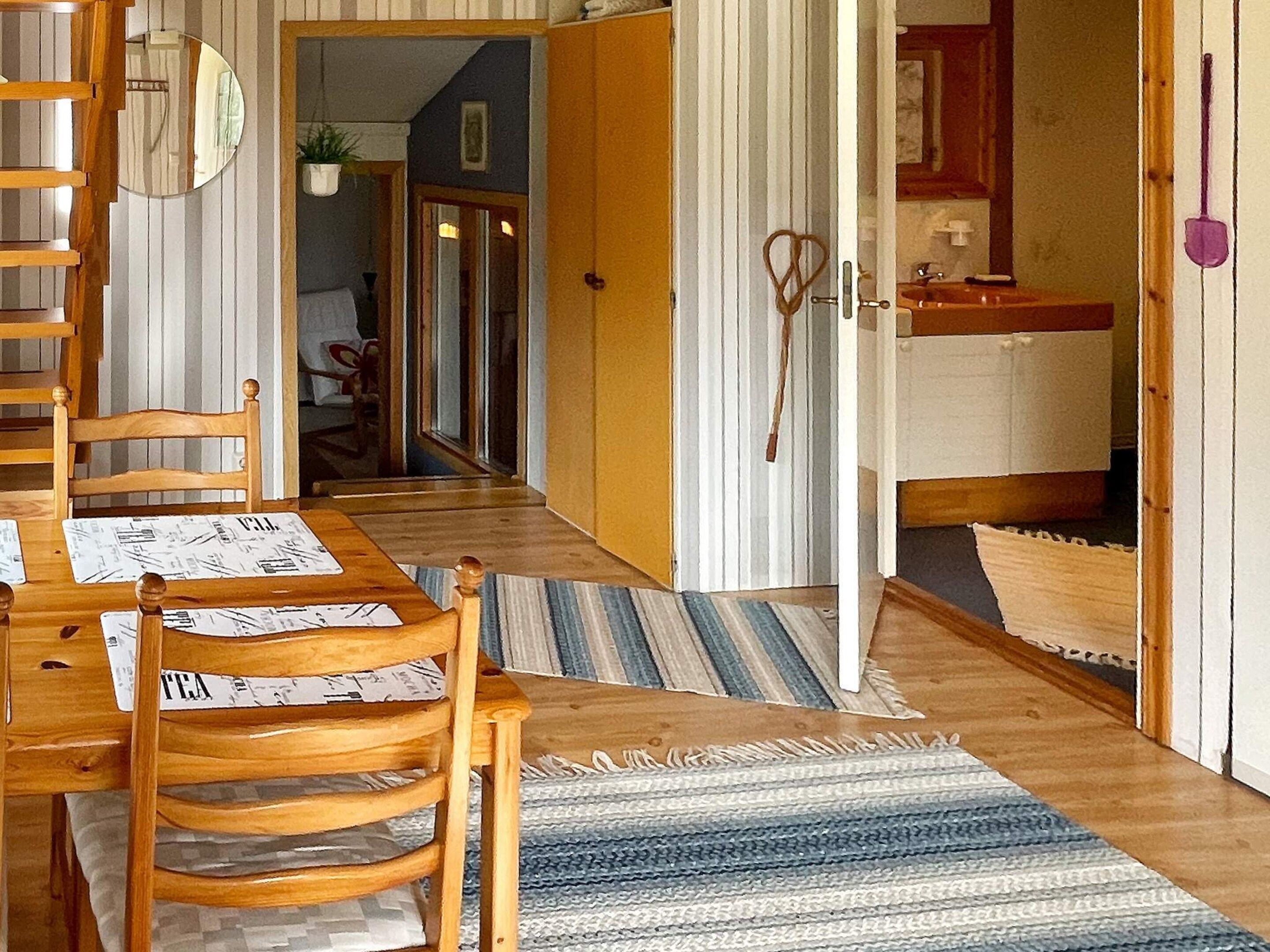 A wooden dining table with chairs, a striped rug, and a kitchen area with a sink and cabinets.
