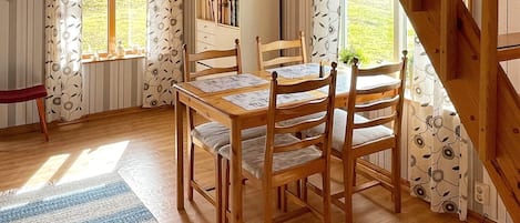 A dining area with a wooden table and chairs, a bookshelf, and a window with curtains.