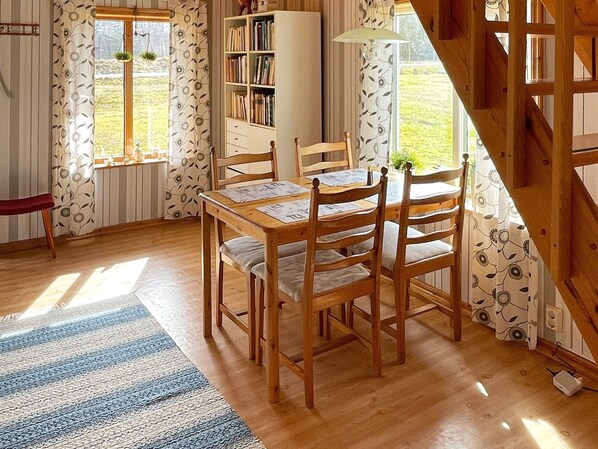 A dining area with a wooden table and chairs, a bookshelf, and a window with curtains. - 4 Person Holiday Home in Holmsjo (Holmsjö)