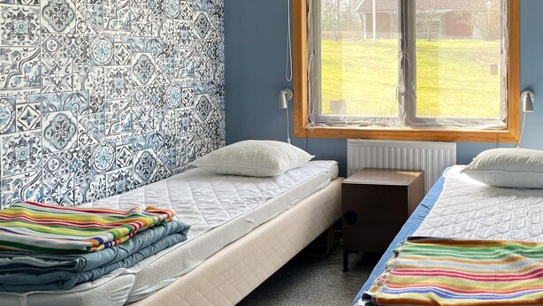 Une chambre avec deux lits, une fenêtre donnant sur un jardin et des carreaux muraux à motifs.
