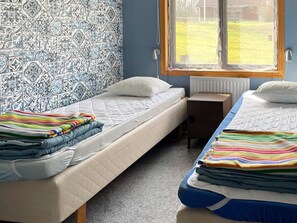 Une chambre avec deux lits, une fenêtre donnant sur un jardin et des carreaux muraux à motifs.