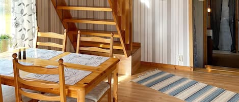 A wooden dining table with chairs, a staircase, and a striped rug.