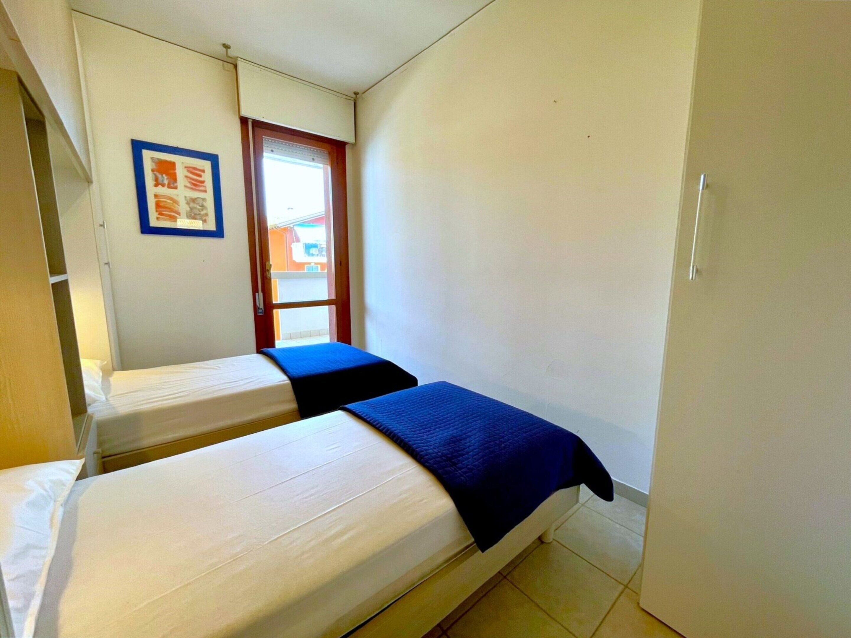 A small, compact room with two single beds, a window, and a door.