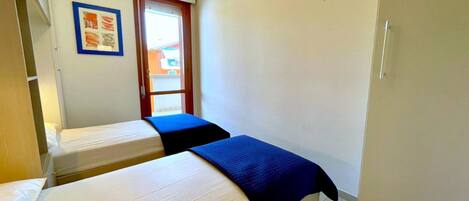 A small, compact room with two single beds, a window, and a door.