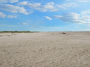 Een breed zandstrand met duinen en een heldere lucht.
