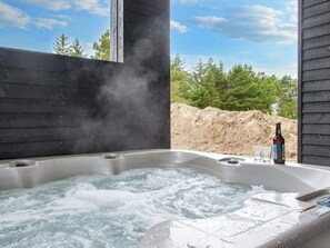 Een hottub met een fles en glazen, omgeven door een houten terras en bomen.
