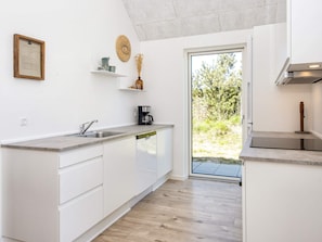 A modern kitchen with white cabinetry, a built-in dishwasher, a coffee maker, and a view of the outdoors. - 5 Star Holiday Home in Romo (Rømø)
