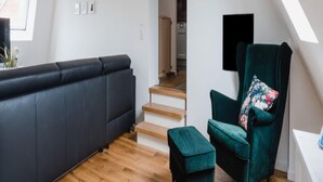 Un salon moderne avec un canapé gris foncé, un fauteuil vert et un petit pouf. Un escalier mène à un niveau supérieur.