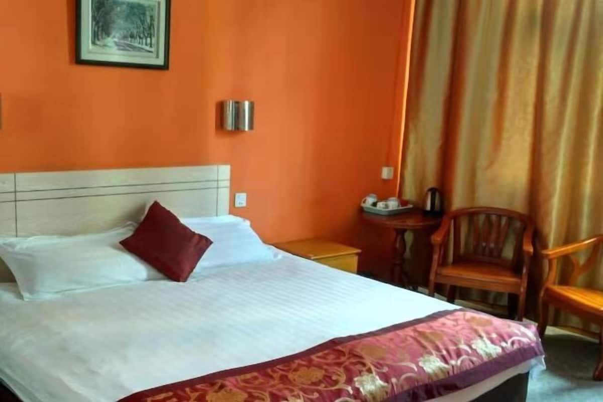 A hotel room with a bed, a nightstand, a chair, and a picture on the wall.