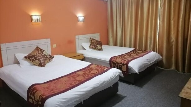 A hotel room with two beds, each with a white mattress and a brown patterned bedspread. There are two wall-mounted light fixtures on the orange walls. - Youxi Sanming Red Lantern Hotel (Youxi)