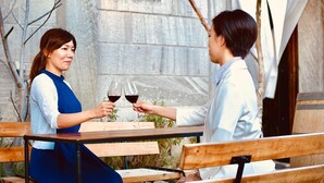 Two people toasting with wine glasses at a wooden table with a stone and iron sign in the background. - Cafe Bar & Inn - Stone and Iron (Otaru)