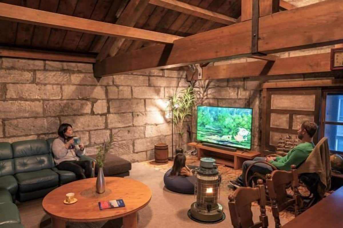 A cozy living room with a stone wall, wooden beams, a television, a coffee table, and a fireplace.