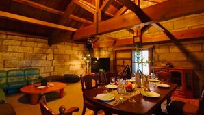 A dining area with a stone wall, wooden beams, a dining table set for four, and a sofa in the background. - Cafe Bar & Inn - Stone and Iron (Otaru)