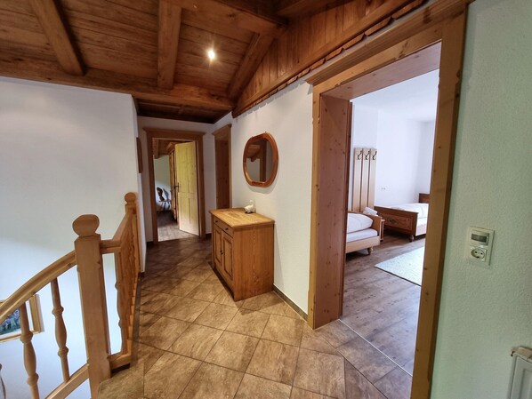 Un escalier en bois mène à une pièce où se trouvent un lit, une table de chevet et un miroir.