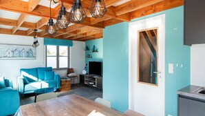 A modern living room with a wooden ceiling, a blue sofa, a dining table, and a kitchen area with a sink. - Holiday Home in Koksijde Near Beach (Koksijde)