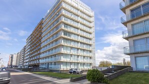 En moderne bygning med flere etager, en glasfacade, et fladt tag og en parkeringsplads foran.