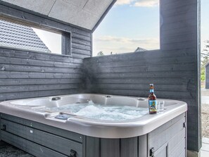 Een hottub met een biertje en glazen, omgeven door houten wanden en een raam.