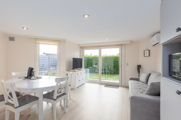 A modern living room with a white dining table, grey sofa, and a TV. - Peacefully Located Holiday Home Near the sea (Middelkerke)