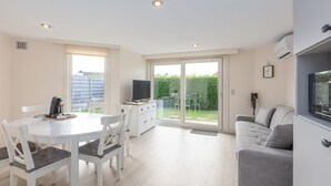 A modern living room with a dining area, a sofa, a TV, and a sliding glass door leading to a garden. - Peacefully Located Holiday Home Near the sea (Middelkerke)