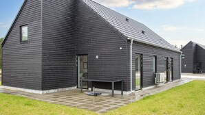 A modern building with a sloped roof, large windows, and a patio area with a table and chairs.
