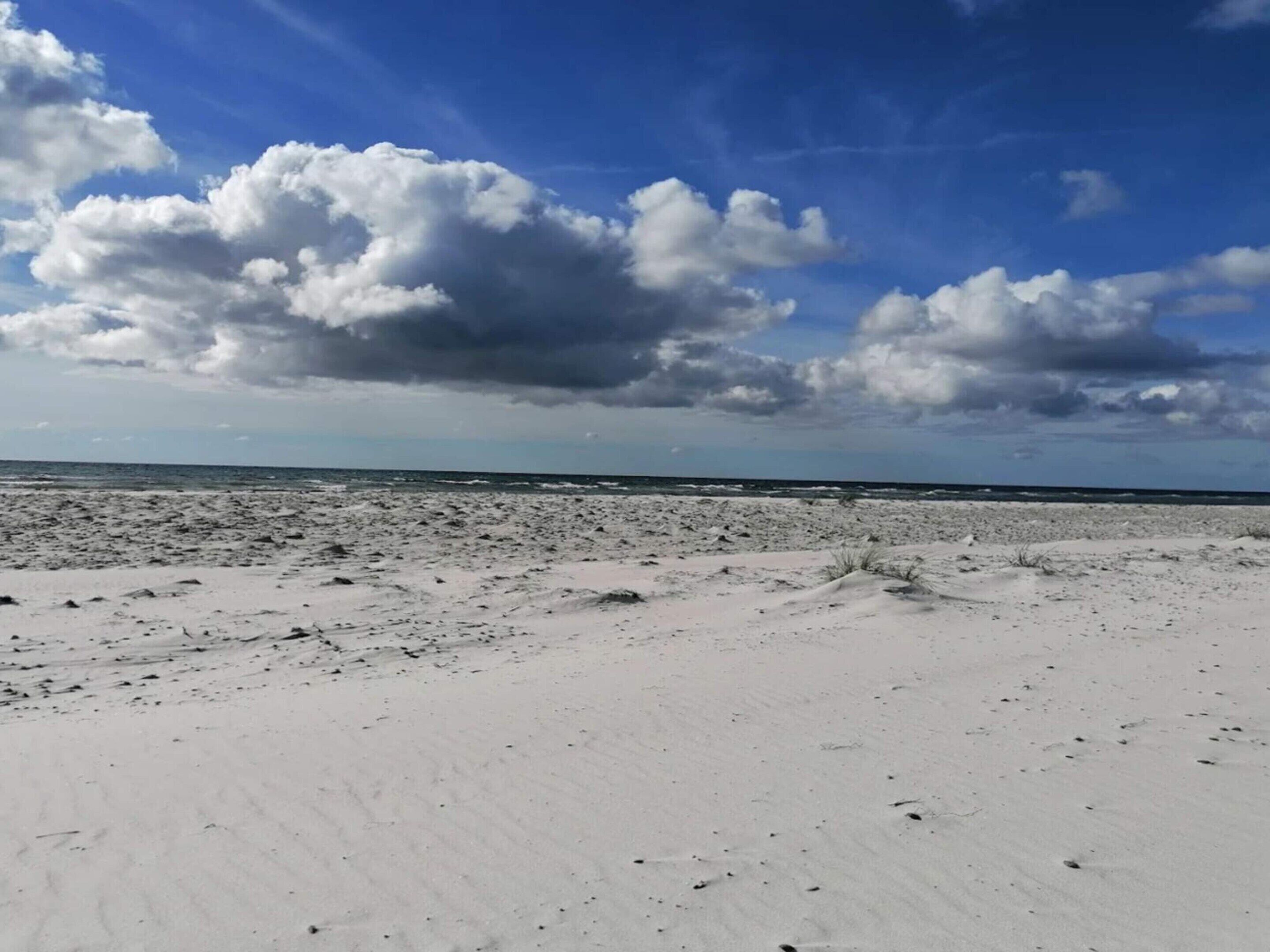 A beach with white sand and a clear sky with clouds.