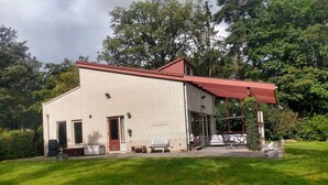 Una casa moderna con facciata in mattoni, tetto rosso e una veranda coperta con mobili da esterno.