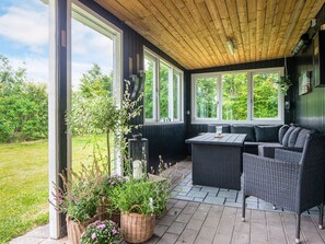 A covered patio with wicker furniture, large windows, and potted plants. - 6 Person Holiday Home in Skjern (Skjern)